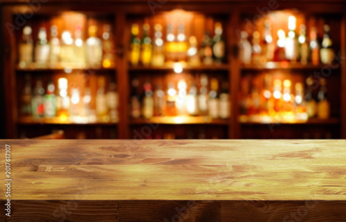 Canvastavla a wooden tabletop in the foreground and a blurred background of a bar with shelv