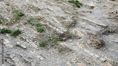 Tableau sur toile Rocky slope with textured sedimentary layers, patches of sparse green vegetation
