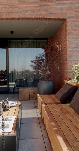 Modern balcony or terrace with wooden furniture, a potted plant, and comfortable seating, perfect for relaxation or outdoor dining.