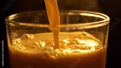 Golden beverage being poured into a clear glass, creating frothy bubbles, dark background, macro shot