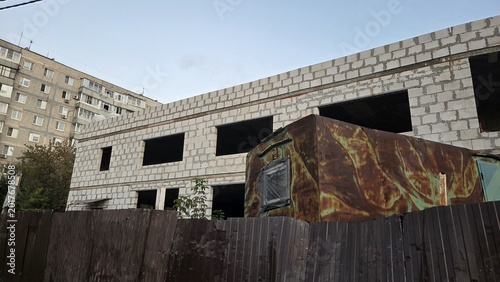 Photos Rusted truck parked behind corrugated fence against unfinished block building fo