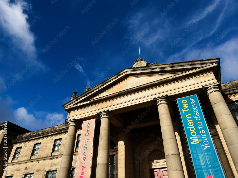 Fototapeta premium Neoclassical Modern Two Dean Gallery museum facade with grand columns and colorful event banners at Modern Two gallery in Edinburgh, Scotland, UK under a dramatic blue sky