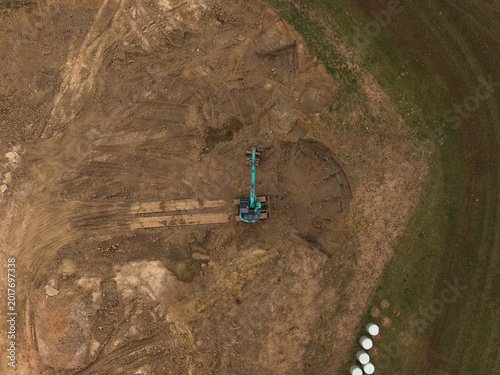 Photos Vertical aerial drone shot of an excavator with raised bucket positioned beside a semicircular excavation area, creating geometric patterns and industrial symmetry at a construction site