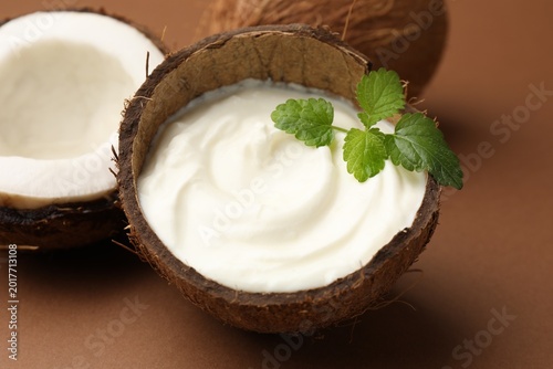 Fotografie Tasty coconut yogurt with melissa leaves in shell and nuts on brown background,