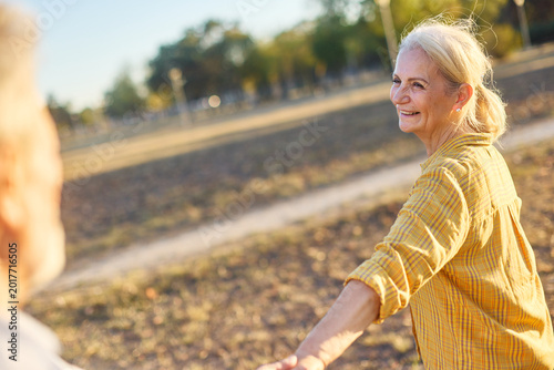 Happy active senior couple, portrait of an elderly woman with her husband dancing or swinging and holding hands in park outdoors