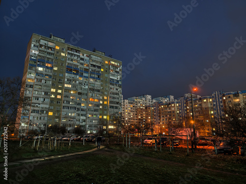 Nighttime cityscape with a glowing apartment buildings, windows lit across multiple floors