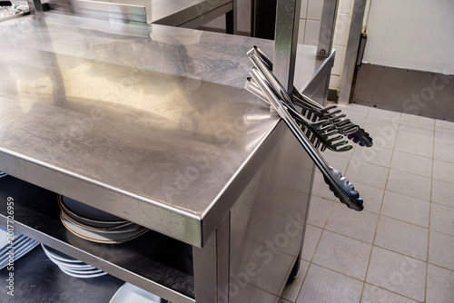 Quadro su tela Two pairs of professional stainless steel kitchen tongs hanging on a commercial