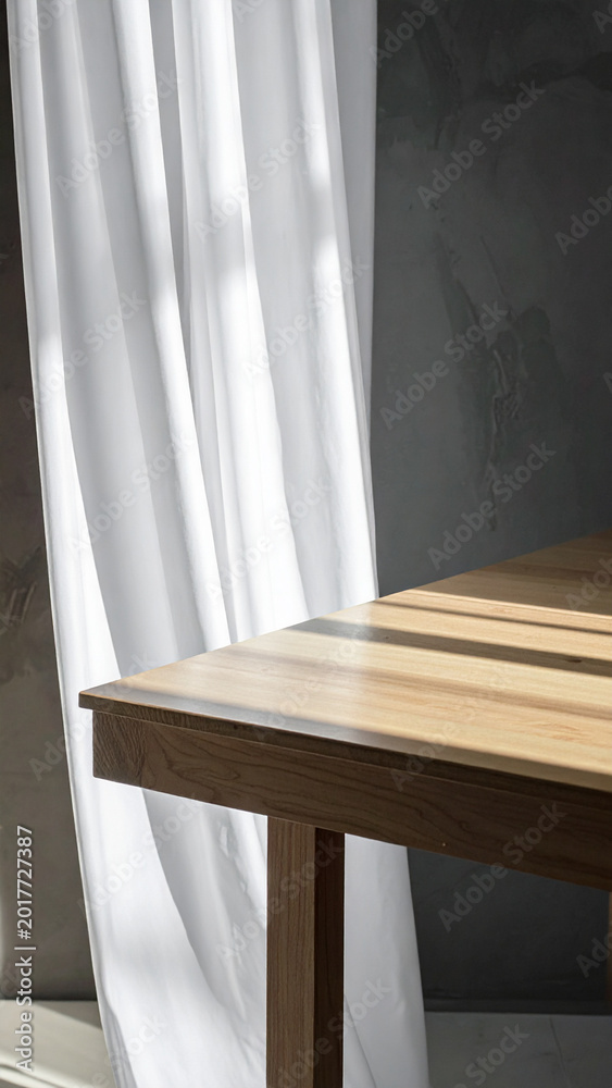 Fototapeta premium Vertical close up of an empty wooden table with warm natural sunlight and shadows from flowing white curtains in a minimalist room for product mockup and organic lifestyle brand photography