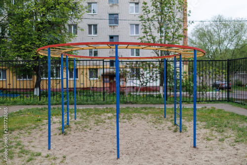 Photography Round colorful monkey bars in a city playground with a brick residential buildin