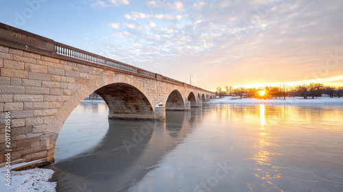 Historic stone bridge at sunset over frozen river with calm winter reflection and golden light