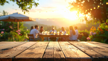 Wooden table top offering copy space with a blurred festive garden party and friends in the background during a golden sunset for outdoor event promotion and summer celebration invitations