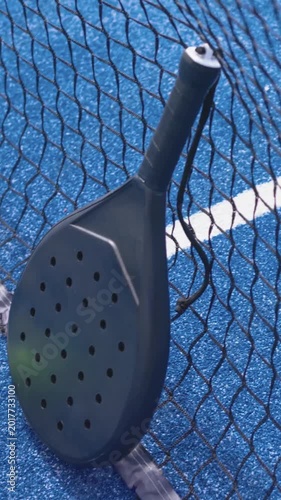Vertical video: Camera pulling back revealing padel racket on net at blue court, green ball resting