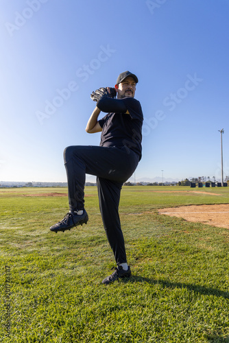 Fotografi Mature man in sportswear standing on pitcher's mound with cap, glove and cleats