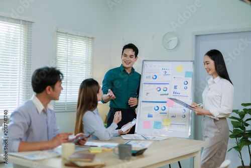 Group of diverse Asian professionals analyzing charts and graphs on a whiteboard, discussing strategies during an office meeting