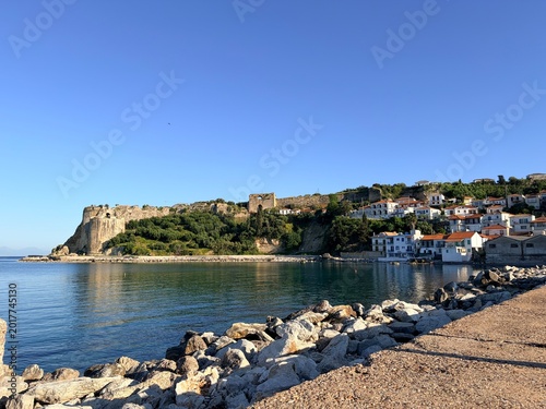 Koroni, Greece, Coastal town with historic stone fortress and red roof houses by calm sea under clear blue sky