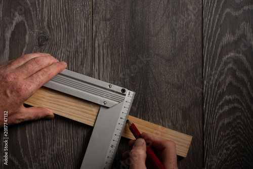 Marking wooden plank with carpenter square and red pencil on dark wood background