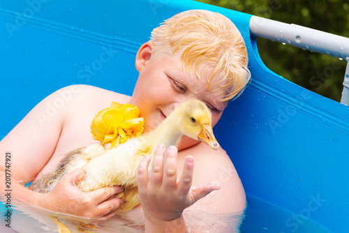 Foto Funny blond boy and gosling in outdoor swimming pool.