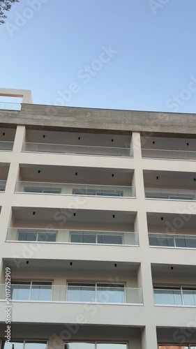 Modern residential apartment building with rows of balconies photographed from ground looking upward against sky. Urban housing facade suits real estate developer ads, mortgage service, investment