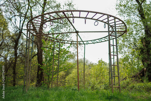 Canvas Print Old rusty round metal monkey bars in an abandoned park surrounded by green trees