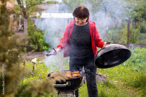 Fotografie Woman checking smoky backyard barbecue grill