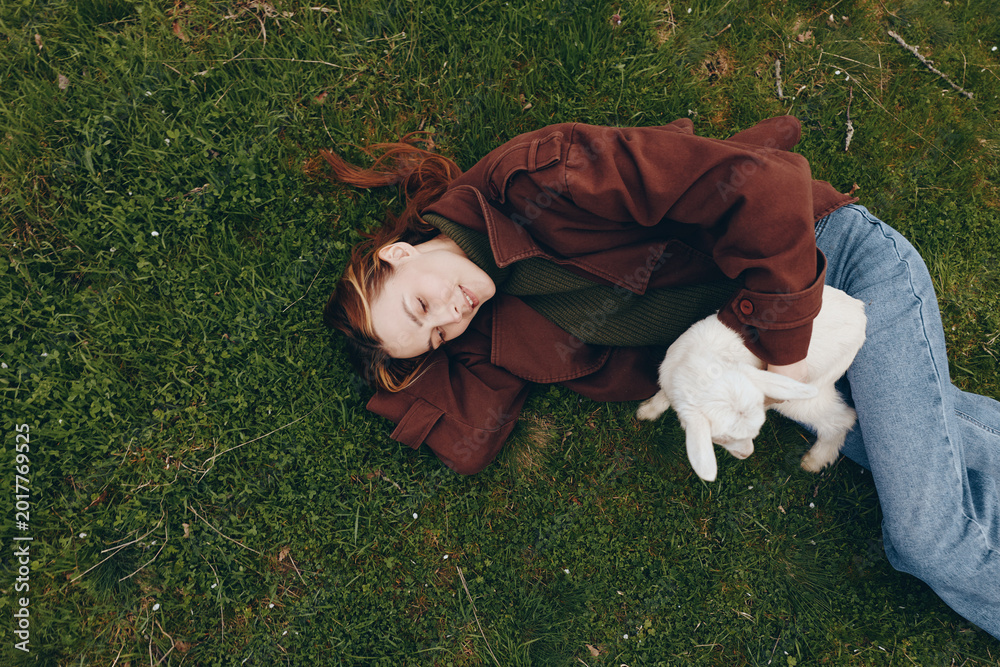 Obraz premium A girl lying on green grass outdoors with a goat kid by her side, a calm lifestyle moment showing companionship, gentle affection, and simple wholesome outdoor life.