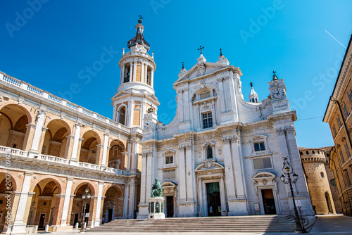 Ornate architecture of the Basilica della Santa Casa di Loreto under a clear sky, showcasing its majestic bell tower, colonnaded facade, and historic details in Loreto