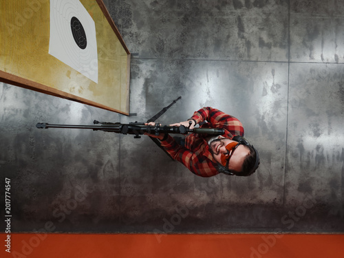 Photos Top Down View of a Focused Marksman with Precision Sniper Rifle and Optical Sight Standing at Indoor Shooting Range