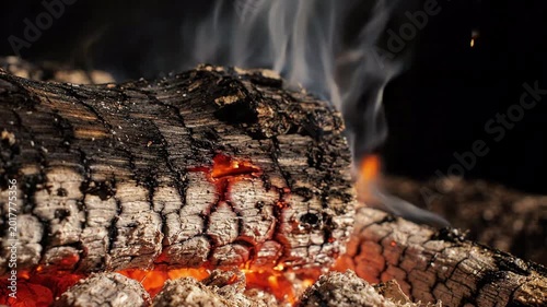 close up of burning wood logs in a fireplace, glowing embers and smoke rising in the darkness, cozy atmosphere, warm lighting