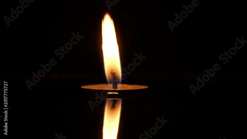 Single candle flame flickering gently on a dark reflective surface, casting a warm glow, atmosphere of peace and contemplation