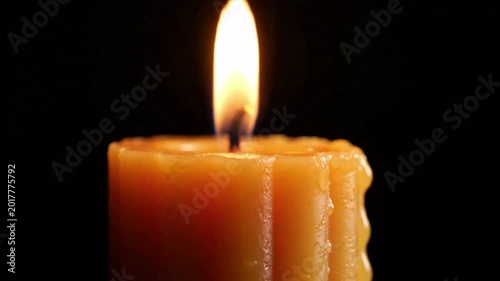 Close-up of a single beeswax candle burning with a warm, bright flame flickering against a dark background, creating a peaceful, ambient atmosphere