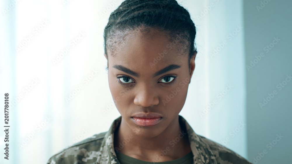 Obraz premium A military personnel looks directly at the camera with focus and determination. The background is simple and light, emphasizing the subject's expression and uniform. The atmosphere suggests readiness.