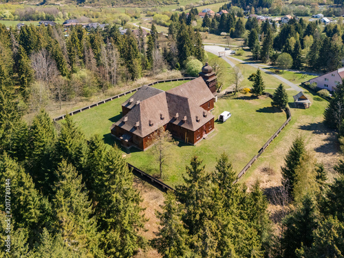 Aerial view of the Wooden Articular Church of Svaty Kriz surrounded by a wooden fence and dense pine forest under a clear sky in Svaty Kriz, Zilinsky kraj, Slovakia.