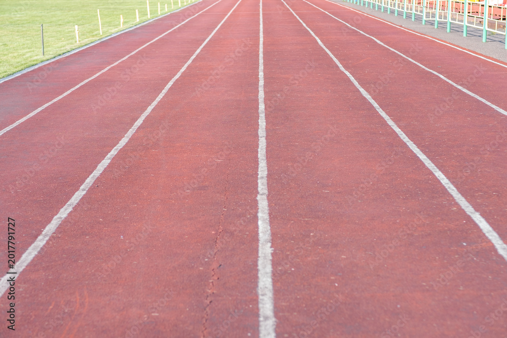 Fototapeta premium Red running track features clearly marked lanes with a green grass field visible in the background, suitable for athletic training and events