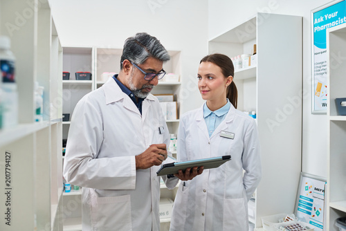 Photography Middle aged Indian man and young woman reviewing tablet in pharmacy, coordinating medication workflow and patient service
