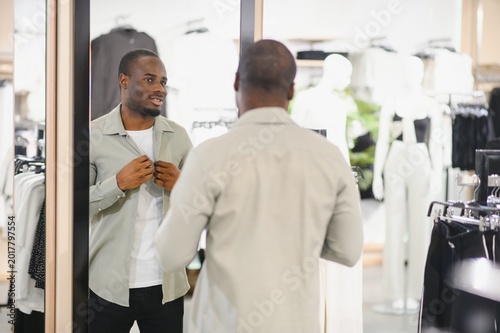 Obraz na plátně Stylish man trying on clothes in a fashion store mirror