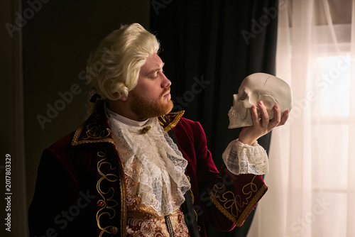 Foto Young man wearing historical costume holding skull and contemplating mortality, referencing Hamlet