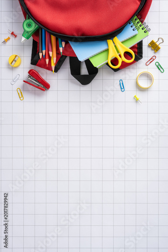 Back to school vertical red backpack with supplies and stationery on grid paper flat lay