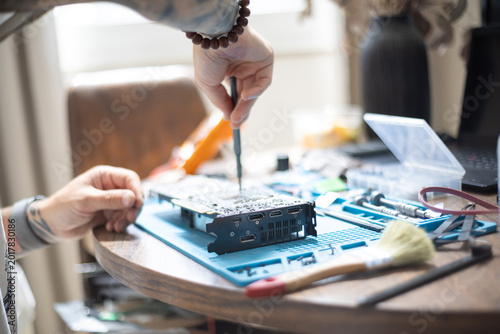 Foto Person repairs a circuit board at a table using tools and supplies in a well-lit