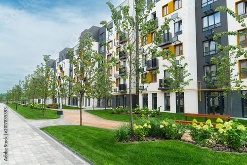 Modern residential complex courtyard with green lawn, trees, benches and new apartment buildings facade, urban landscape property real estate concept