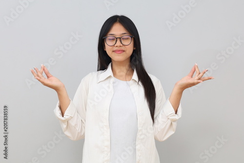 Photo of a young woman smiling with her eyes closed, doing a yoga pose, meditating with deep breathing, feeling relaxed, wearing casual clothes, standing isolated on a white background.