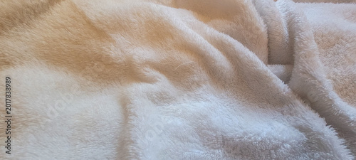 Cream fluffy textile background with soft folds, microfiber texture, warm lighting, cozy bedding aesthetic, and comfortable fabric composition.