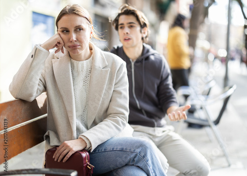 Tableau sur toile Young man sits on street bench with upset woman and apologizes to her