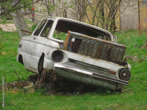 A weathered white vintage car shell abandoned and decaying in a grassy rural backyard