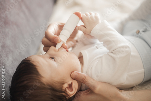 Close-up of an adult administering nasal drops to a baby using a white spray bottle at home.