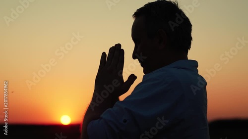 Christian man praying at dawn, close-up. Man confesses. Faith in God. Man prays family children against backdrop sky sun. Relaxation meditation nature. Apologizing. Hope. People religion. Silhouette