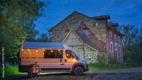 Foto white camper van with night illumination in from of facade of old stone house in
