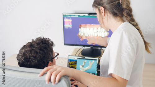Fotografía Dentist pointing at a computer screen showing a 3d model of teeth, explaining a