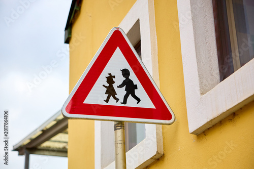Triangle traffic sign with children silhouette near yellow building wall