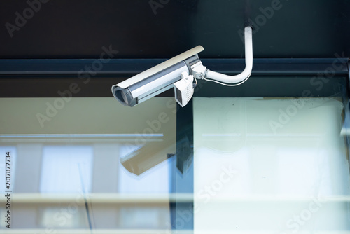 Konstfotografi Security camera mounted on a building exterior, positioned above a glass window,
