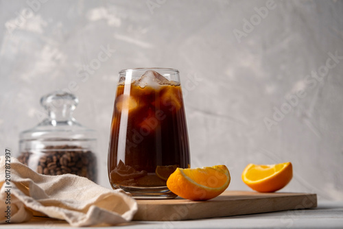 Coffee with orange juice bumble in a tall glass with ice on a light background with coffee beans, fruits and morning shadows
